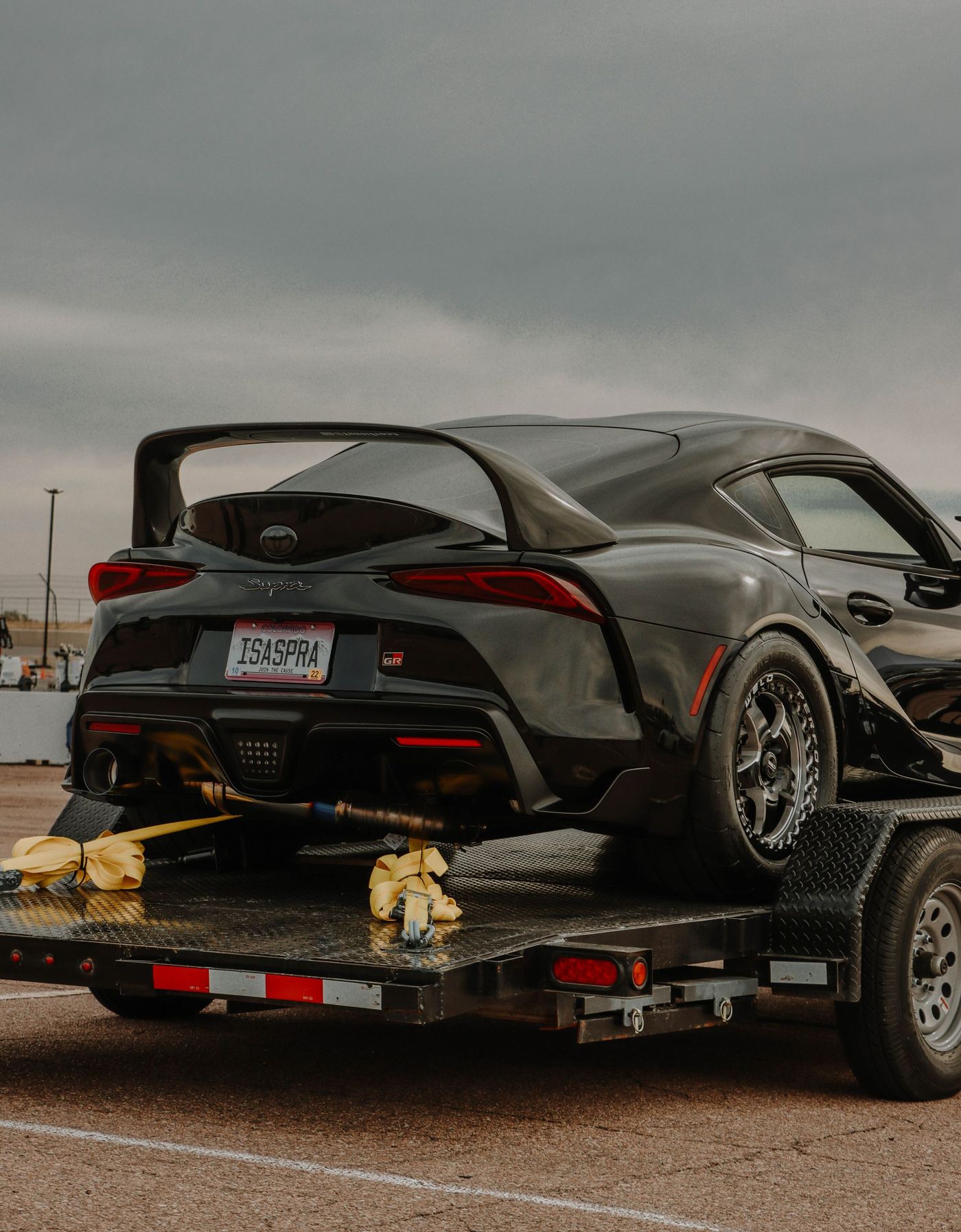 A single sports car strapped down on an open two-car trailer, tie-downs across the wheels.